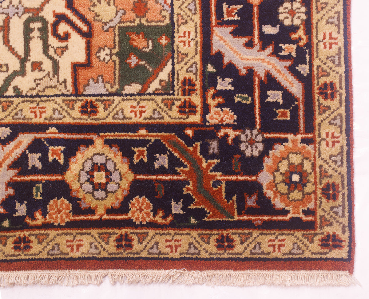 A close-up of a Handmade Indo Heriz carpet corner showing a dark navy field with beige, rust, and green geometric motifs, a decorative border, and cream fringe.