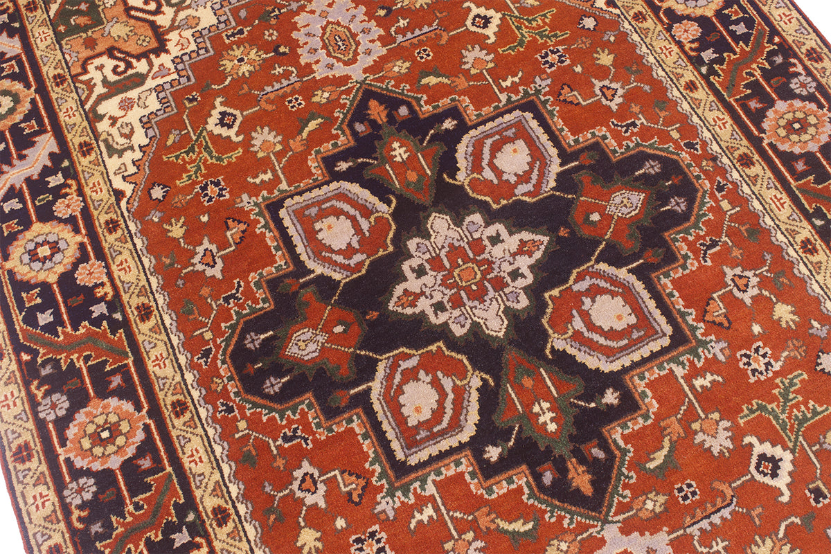 A close-up view of a traditional Handmade Indo Heriz carpet with a warm rust-red field, dark navy medallion, and cream floral details.