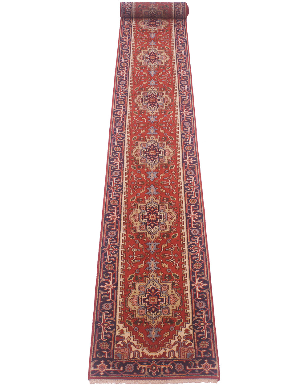 A 7.5m long, narrow traditional Heriz runner rug shown flat against a plain white background. The rug has a deep red field with ornate central medallions and borders in navy blue, beige, and muted gold tones.