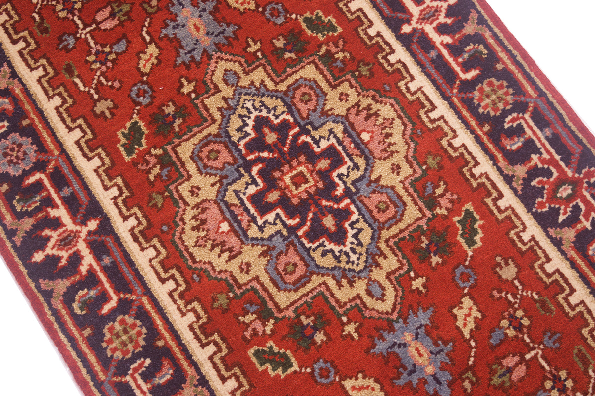 A close-up of a traditional Indian Heriz runner with a red field, beige and navy blue borders, and a central medallion pattern.