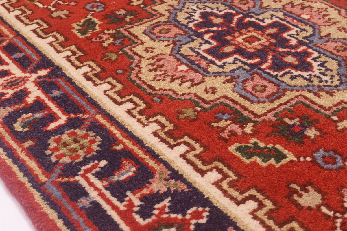 A close-up of a traditional patterned Indo Heriz runner rug with a red field, beige borders, and navy blue geometric motifs.