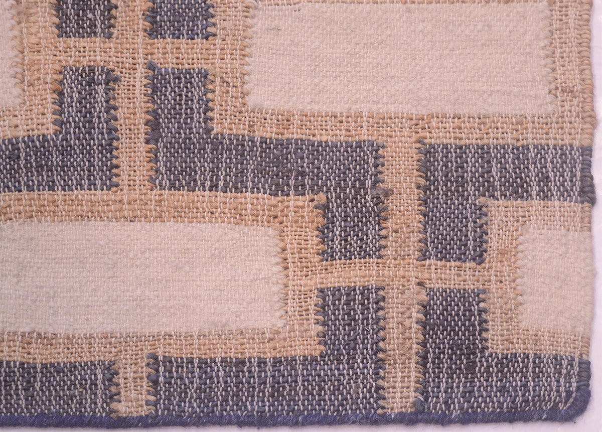 Close-up of a woven textile pattern with alternating cream and slate blue-gray geometric blocks separated by tan lines.