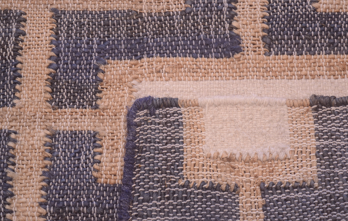 A close-up of a woven textile with a geometric patchwork pattern in beige, taupe, and slate blue-gray.