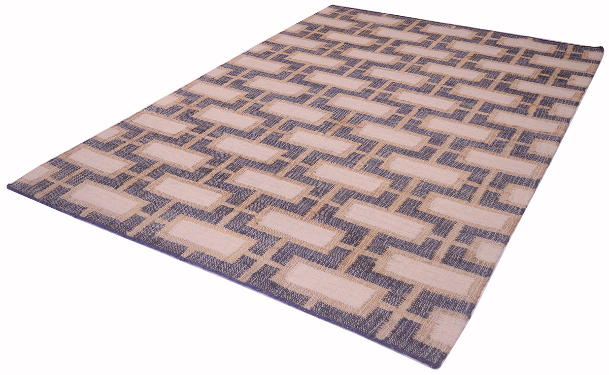 A rectangular area rug with a geometric pattern of beige rectangles on a navy blue background, shown at an angle on a white background.