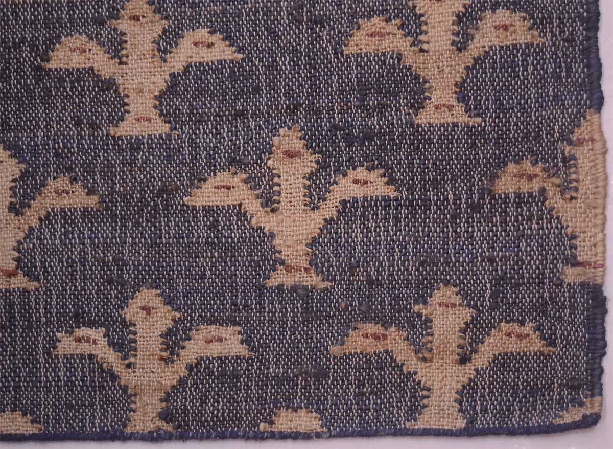 A close-up of a woven textile showing a repeating stylized fleur-de-lys pattern in tan/beige on a dark blue background.