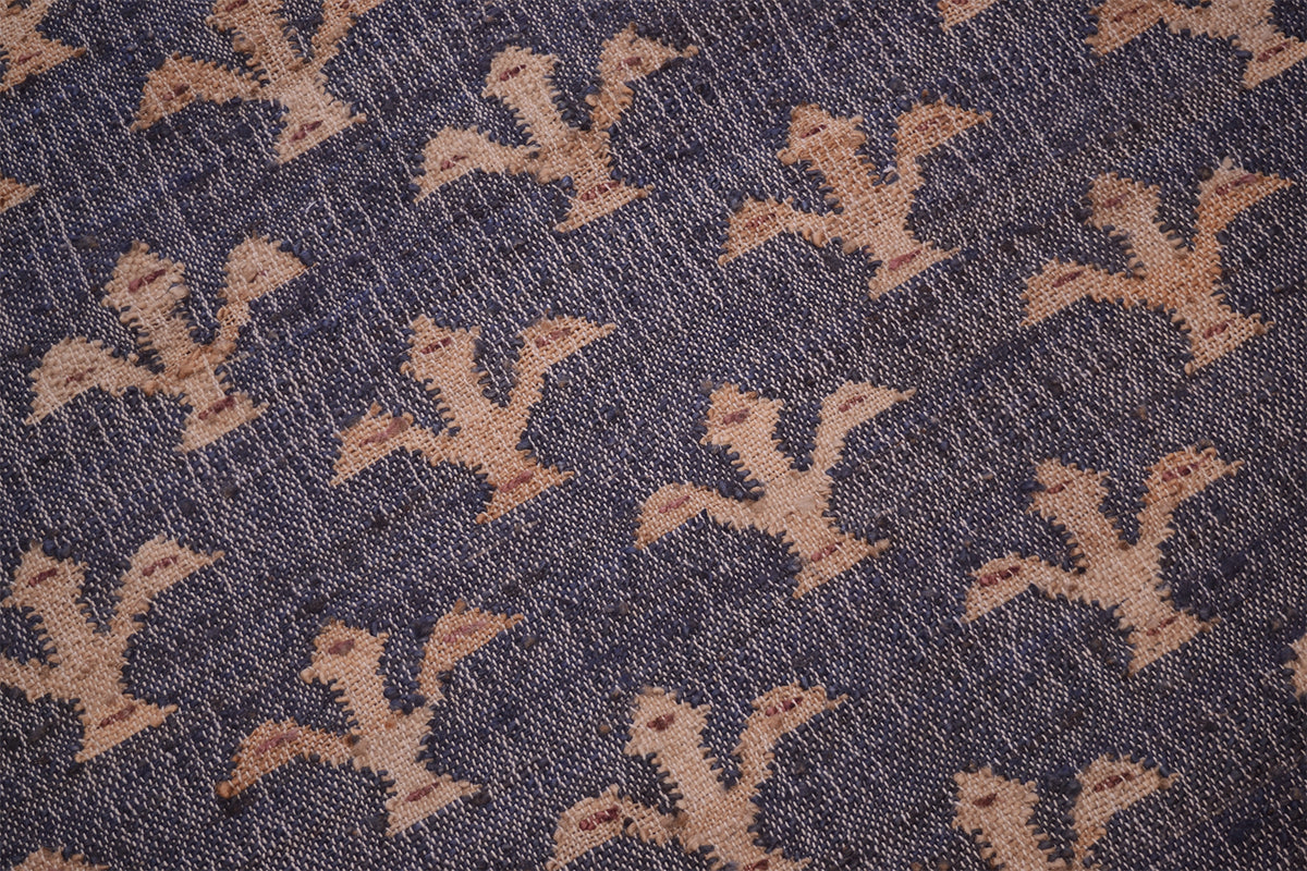 A close-up of woven jute rug with a repeating tan floral pattern on a dark navy blue background.