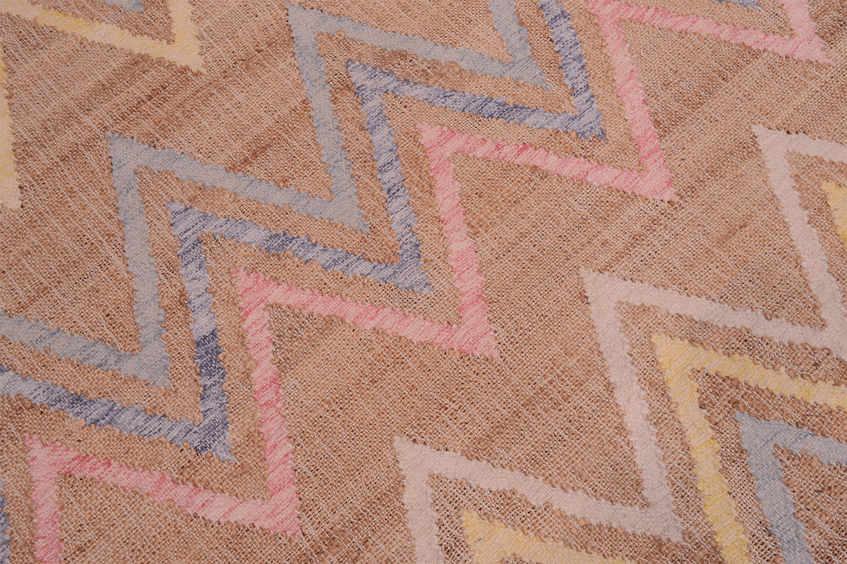 A close-up of a woven textile with a zigzag chevron pattern in muted pink, dusty blue, pale yellow, and beige tones.