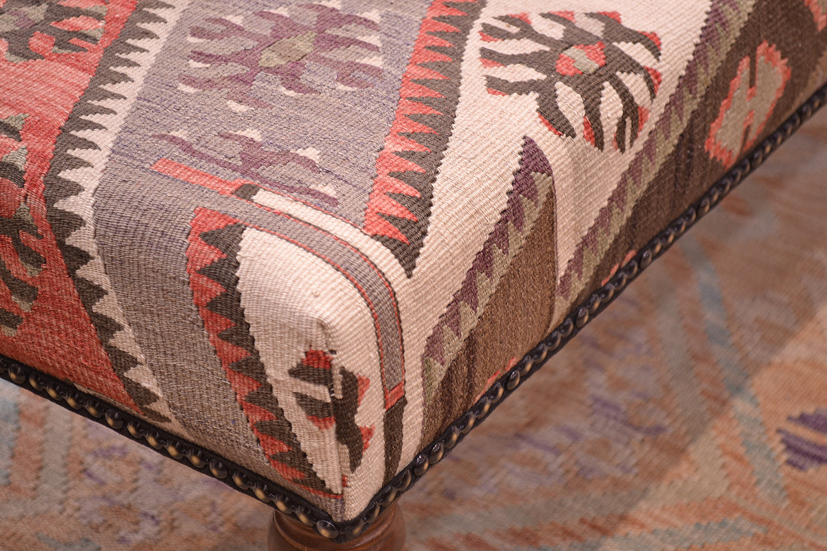 Corner detail of kilim bench stool with geometric patternging with vntag turksih kilim with cream, brown, terracotta, mauve and greys. with beaded edging. Placed on an Afghan soft wash handmade kilim.