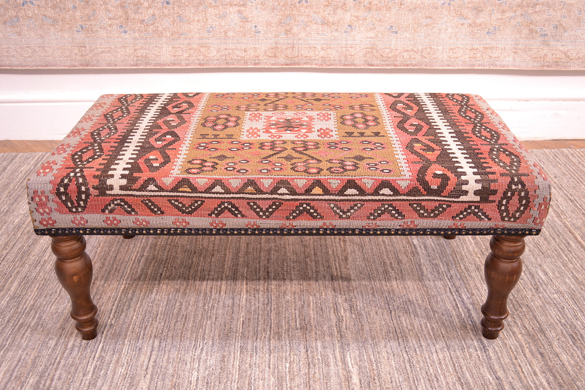 Side view of anatolian kilim long bench with geometric design with rose terracotta, cream, soft brown and blue grey with centralised floral geometric medallion with a light olive green. Placed on a afghan neutral handmade rug.
