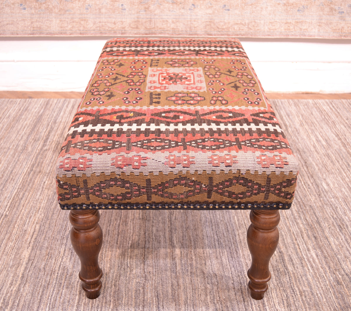 End view of kilim bench upholstered with a vintage kilim with softened colours of light olive green, soft grey blues, rose terracottas and soft brown with white highlights. Placed on a neutral afghan handmade carpet.