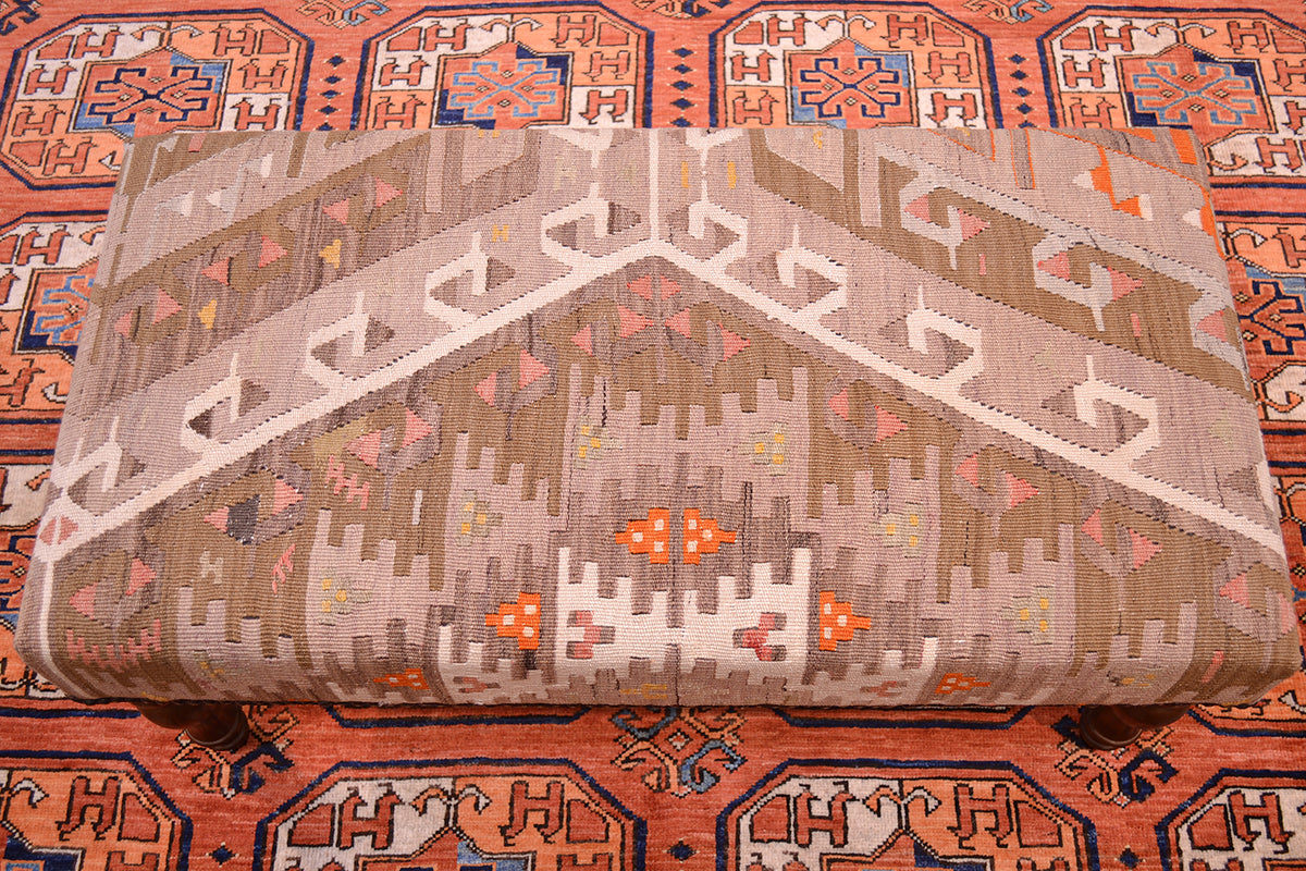 View of geometric patterning of kilim bench stool with muted softened pastel tones of vintage turkish kilim. Place on a terracotta afghan carpet.