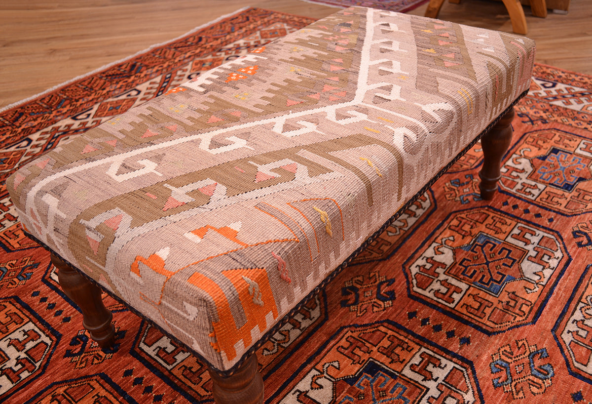 Size view of kilim bench upholster with vintage turkish kilim with colours of soft beige, light olive green, orange and coral pinks. Placed on a fil pai design afghan carpet in terracotta tones.