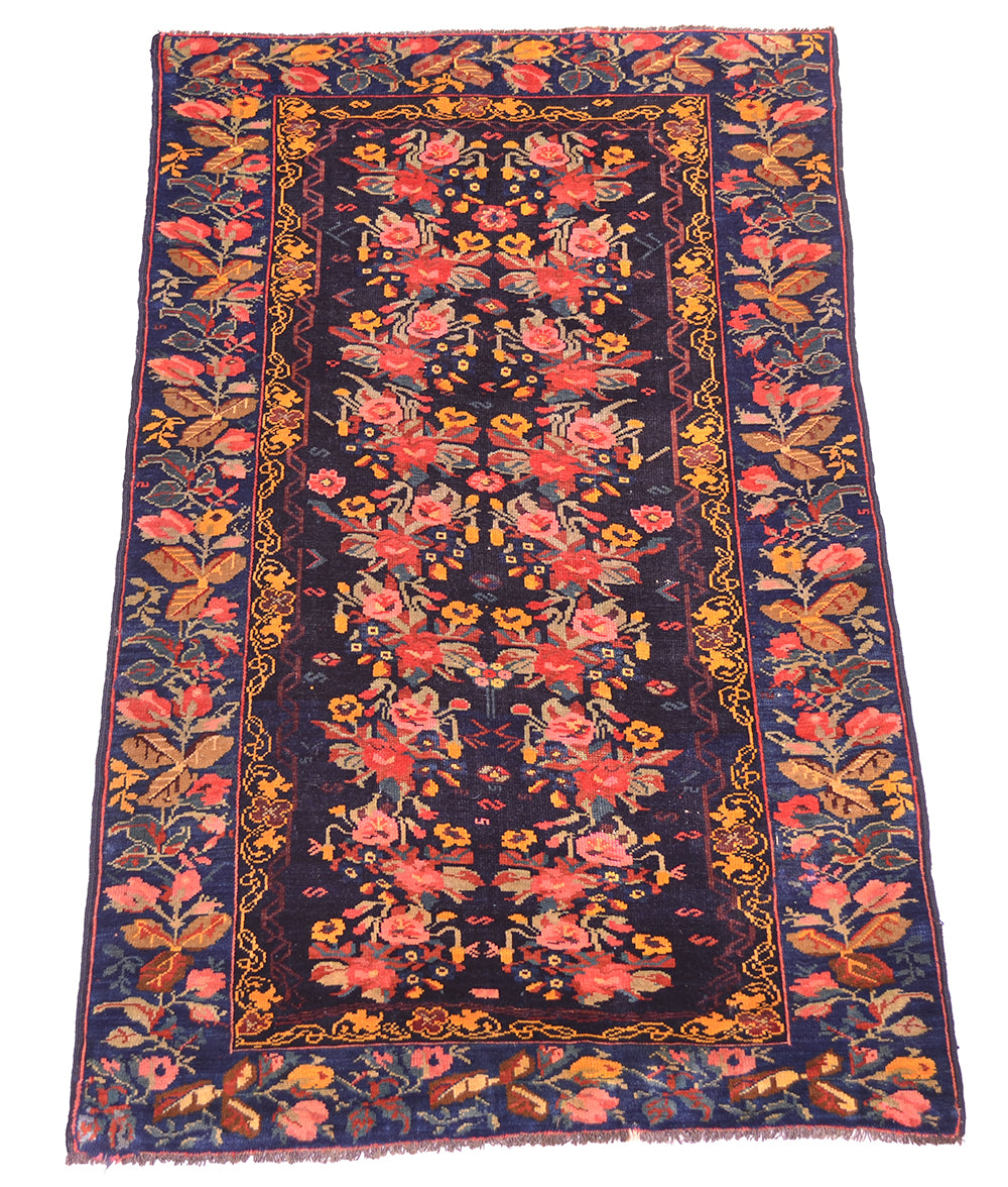 Overall view of antique karabagh rug with deep contrasting dark indigo filed wth multiple florals in field and border and gul farang design with pinks and golds and light greens with flourishing floral border.