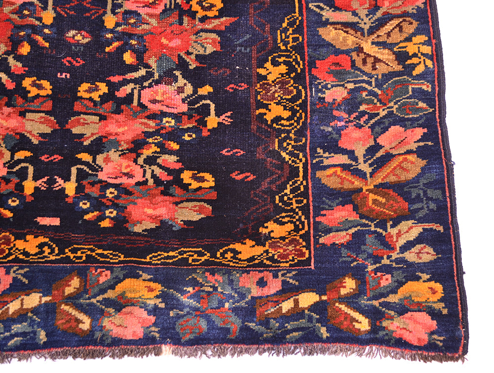 Corner detail of antique floral rug placed on a white background with deep blue border with floral decorative rose and flower motifs and floral filled main field with deep indigo ground.