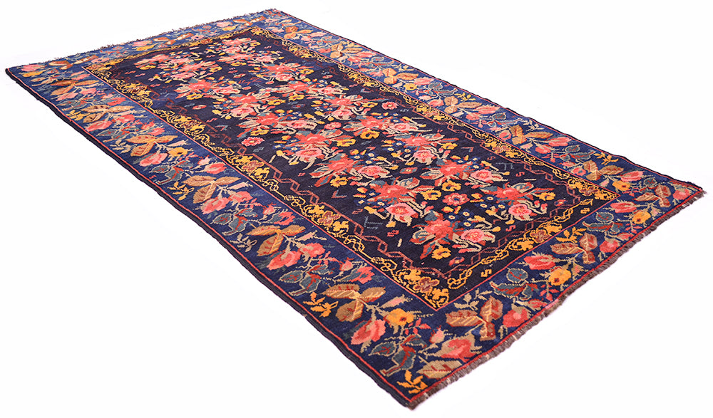 Angled view of Antique Karabagh carpt with gul farang design with blue gorund border and deep blue black field. Placed on a white background. Roses and rose leaves border with intricate scrolling vines inner border.....All over floral design with naturalistic clours.