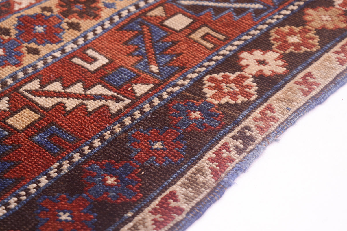 A close-up of an authentic Caucasian geometric Kuba region antique Karagashli rug with red, blue, beige, and brown woven motifs, shown on a plain white background.