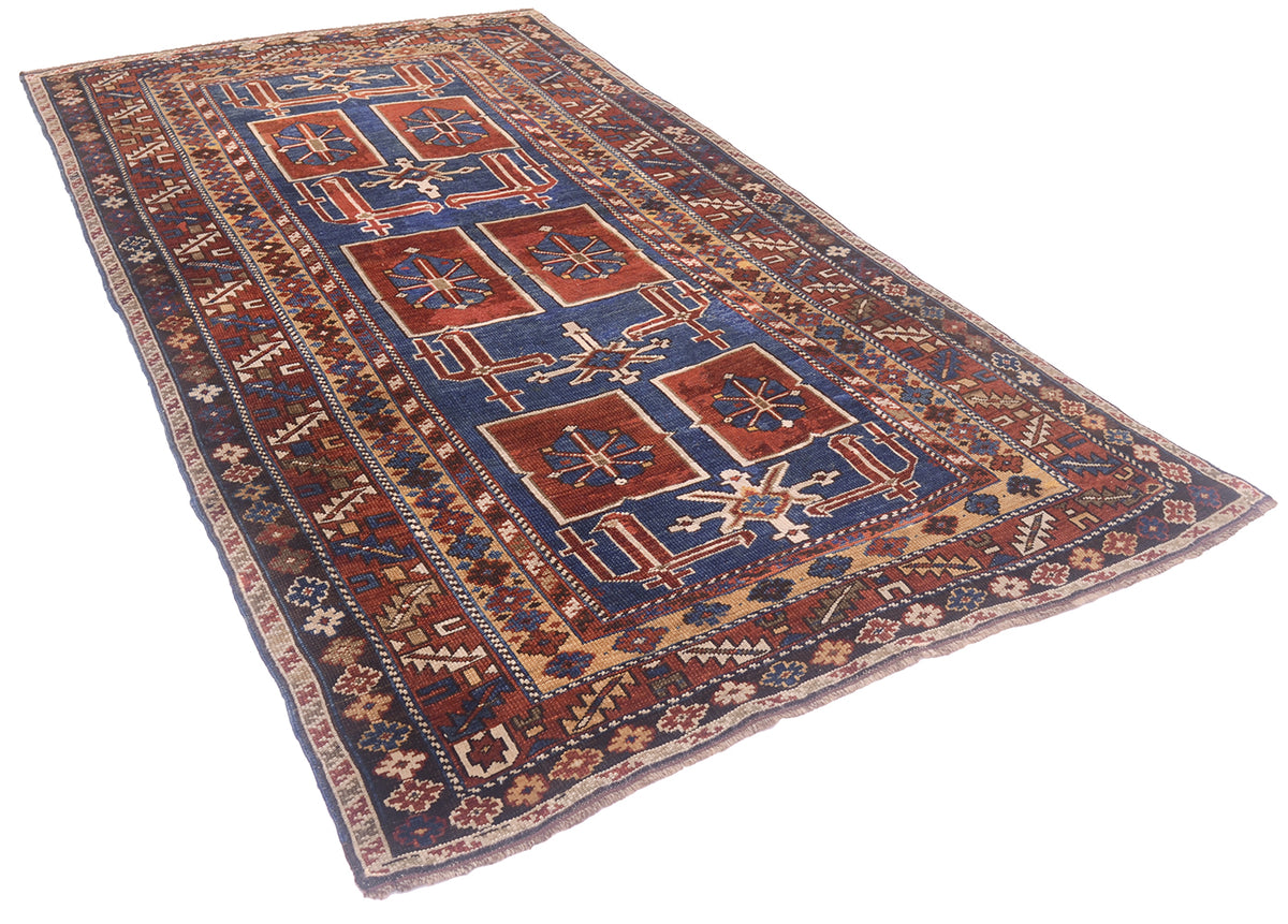 A traditional Caucasian Antique Karagashli rug with a geometric pattern, featuring a navy blue field, rust red squares, and beige borders, shown on a plain white background.