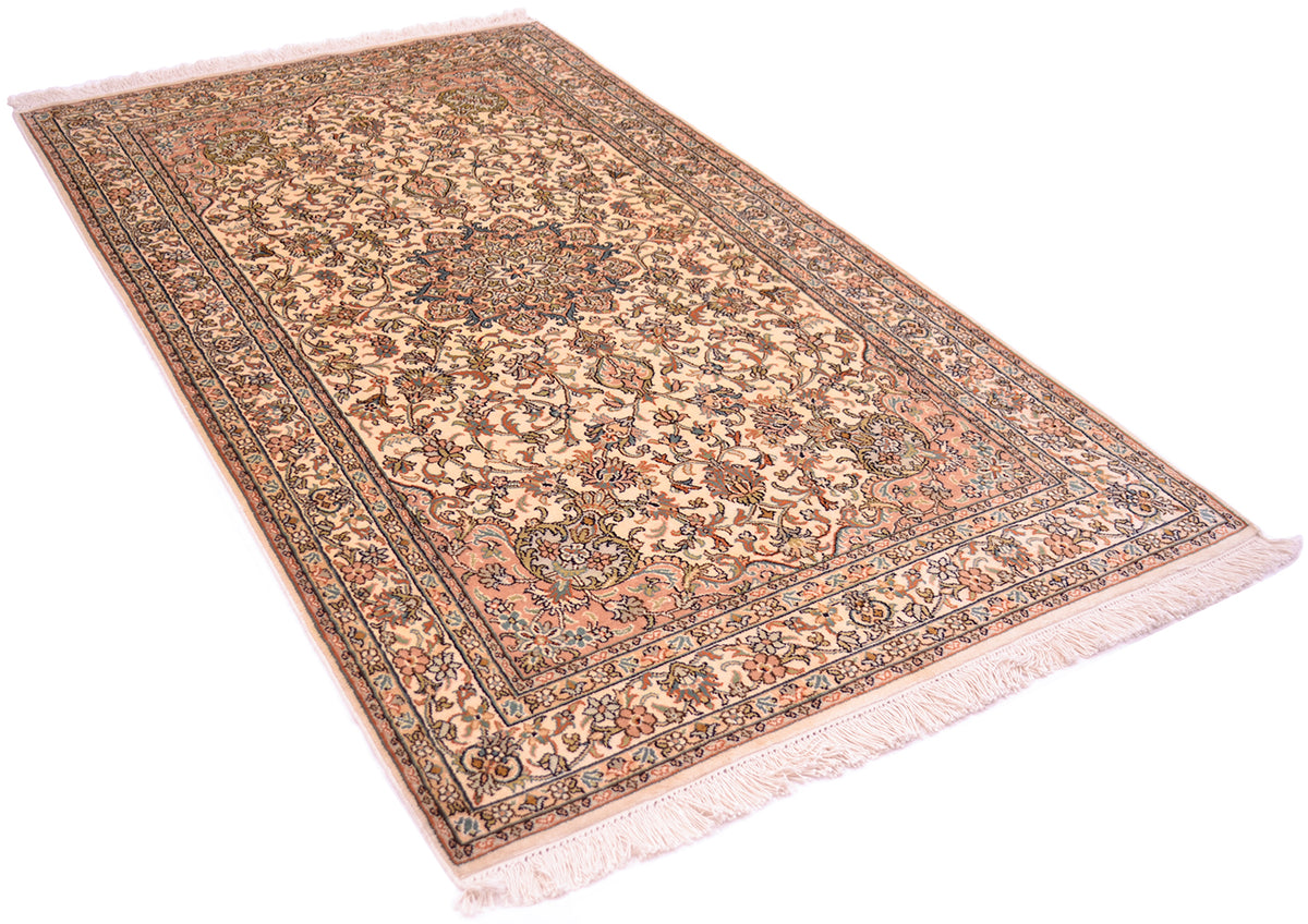 A fine silk rug with a traditional floral pattern, featuring a central medallion, decorative borders, and cream-colored fringe on the ends, shown against a plain white background.