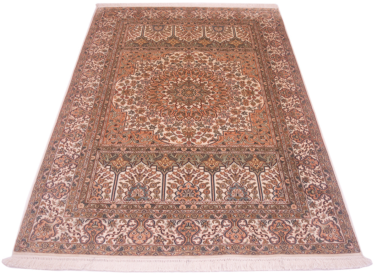 A silk Kashmir rug with an intricate floral pattern in shades of terracotta, beige, brown, and muted blue, featuring a central medallion and fringes