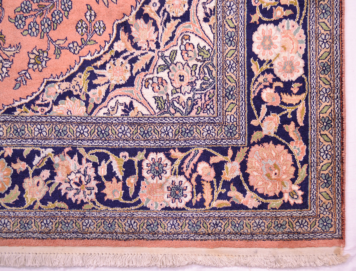 Close-up of an ornate silk Kashmir area rugs corner showing a navy blue border with peach, cream, and green botanical motifs and a fringed edge.