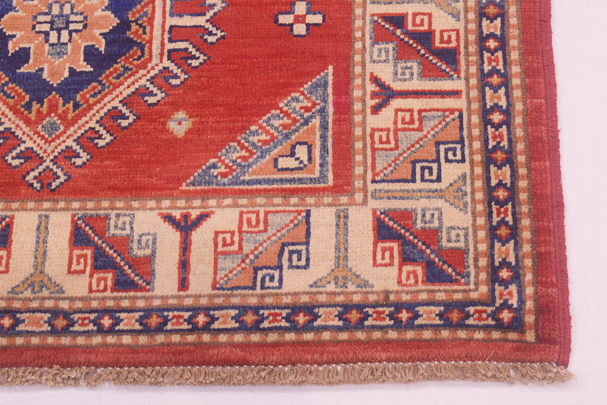 Close-up of red Kazak rug corner with blue geometric panel and border trim