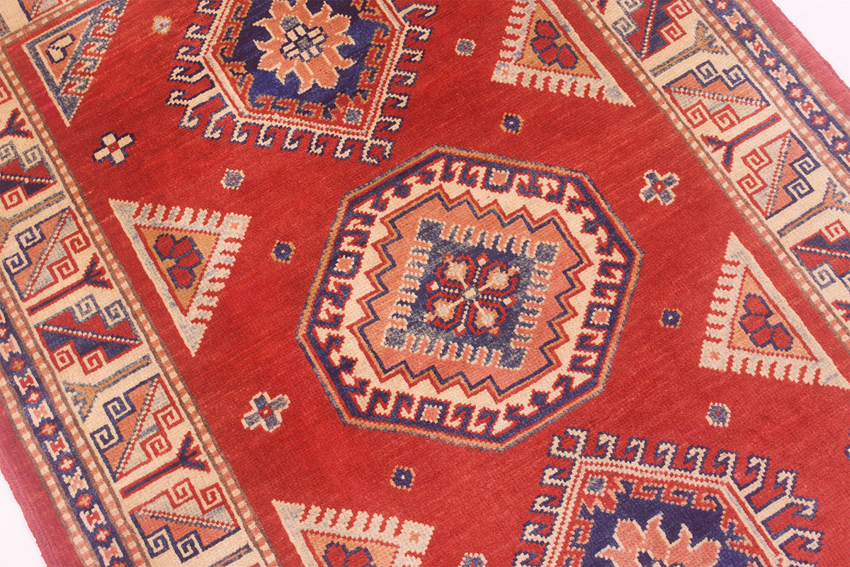 Close-up of red Kazak rug with central floral medallion and multicolor details