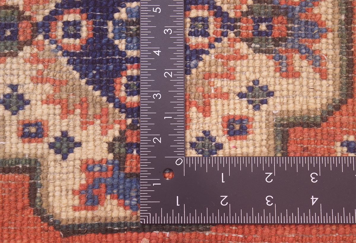 Close-up of the knotted back of ornate small size handmade Kazak Mat with a dark metal L-square ruler and measuring tape placed over it to show scale, showing the rug's cream, rust red, and navy blue woven design.