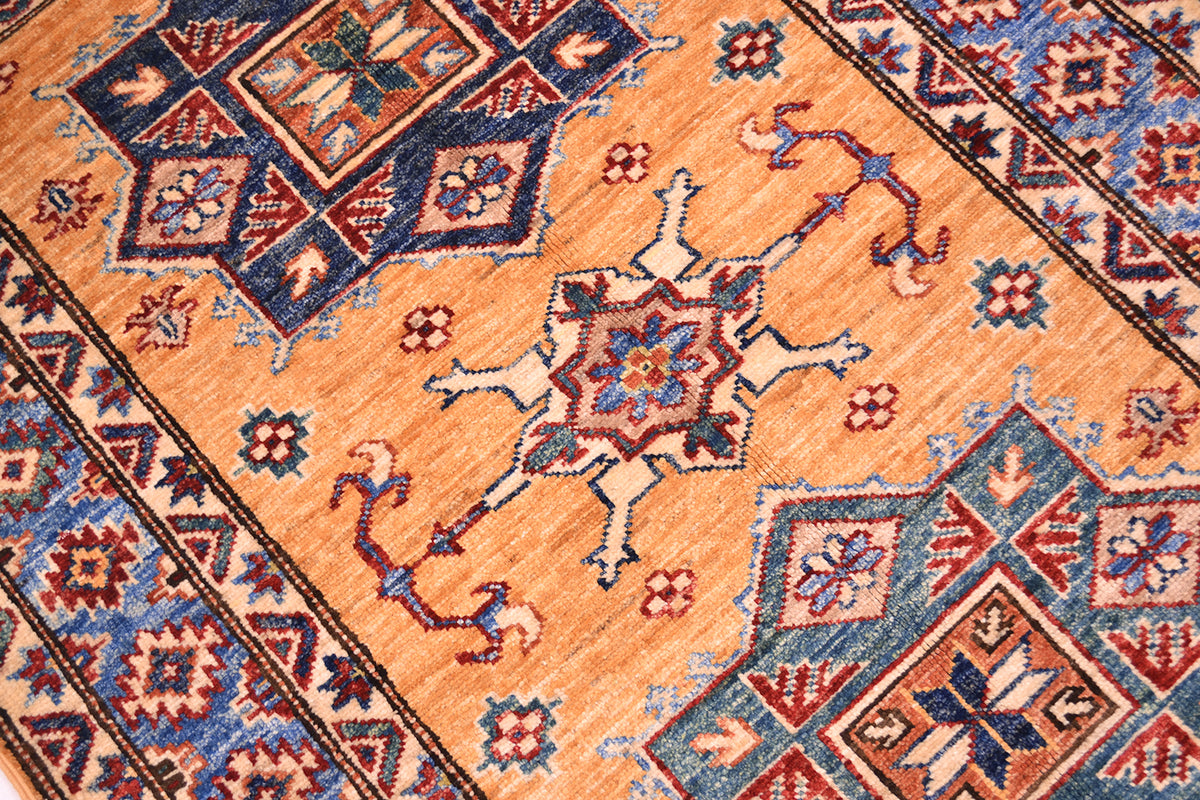 A close-up of a traditional handwoven small fine Afghan Kazak rug with a warm amber yellow field, featuring a central starburst medallion and geometric borders in navy blue, rust red, and cream.