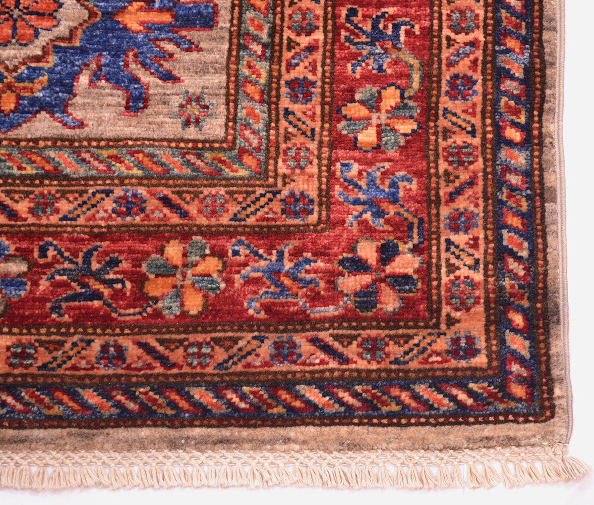 Close-up of a handmade Afghan Kazak Runner corner showing a red field with floral motifs, blue and orange accents, beige and brown borders, and cream fringe.