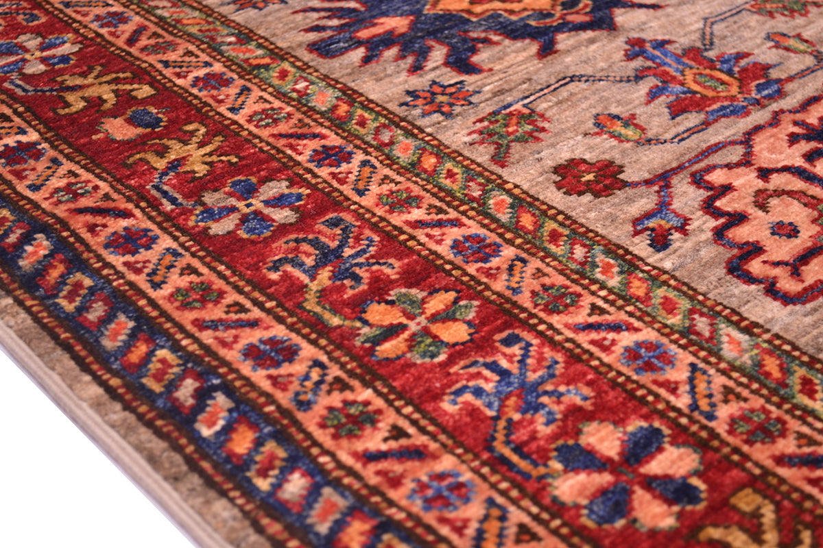 A close-up of a traditional patterned Afghan Kazak Runner showing detailed woven motifs in red, blue, grey, and orange.