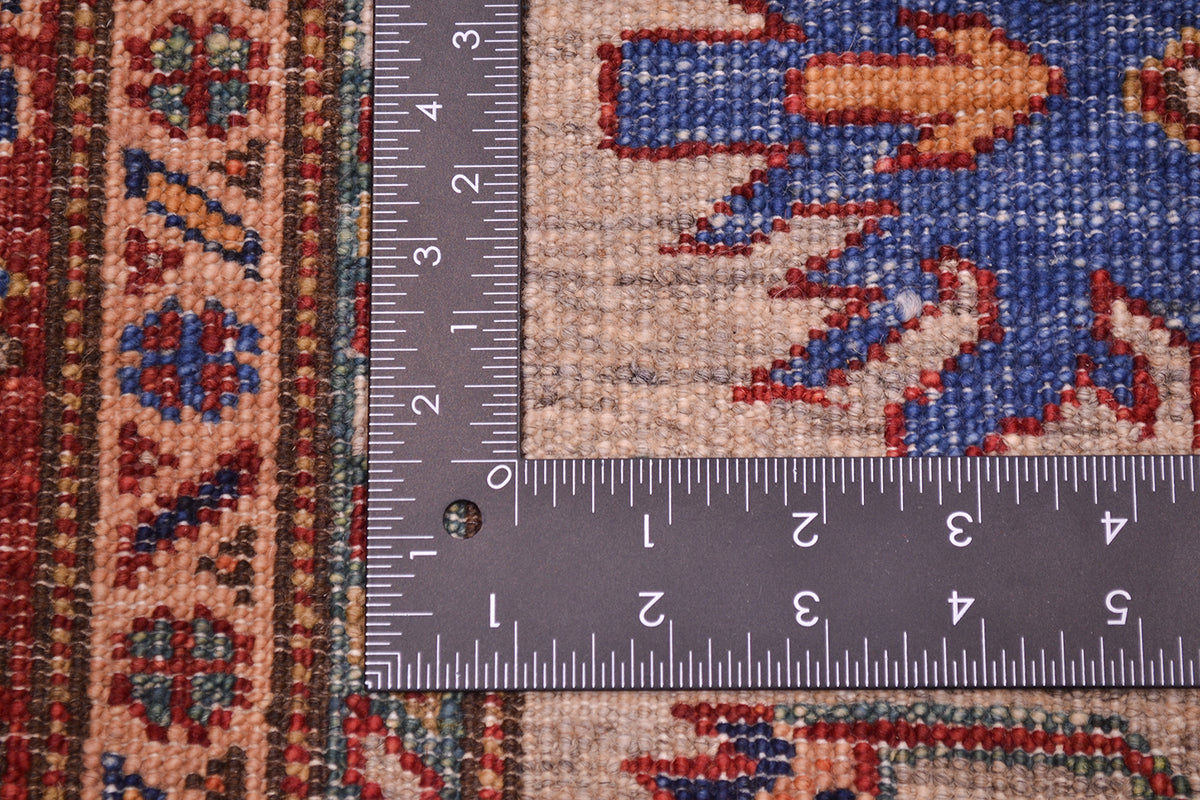Close-up of the knotted weave of a patterned Afghan handmade fine Kazak Runner with a metal ruler placed along the edge to show scale, featuring a grey field with blue, red, and orange motifs and a decorative border.