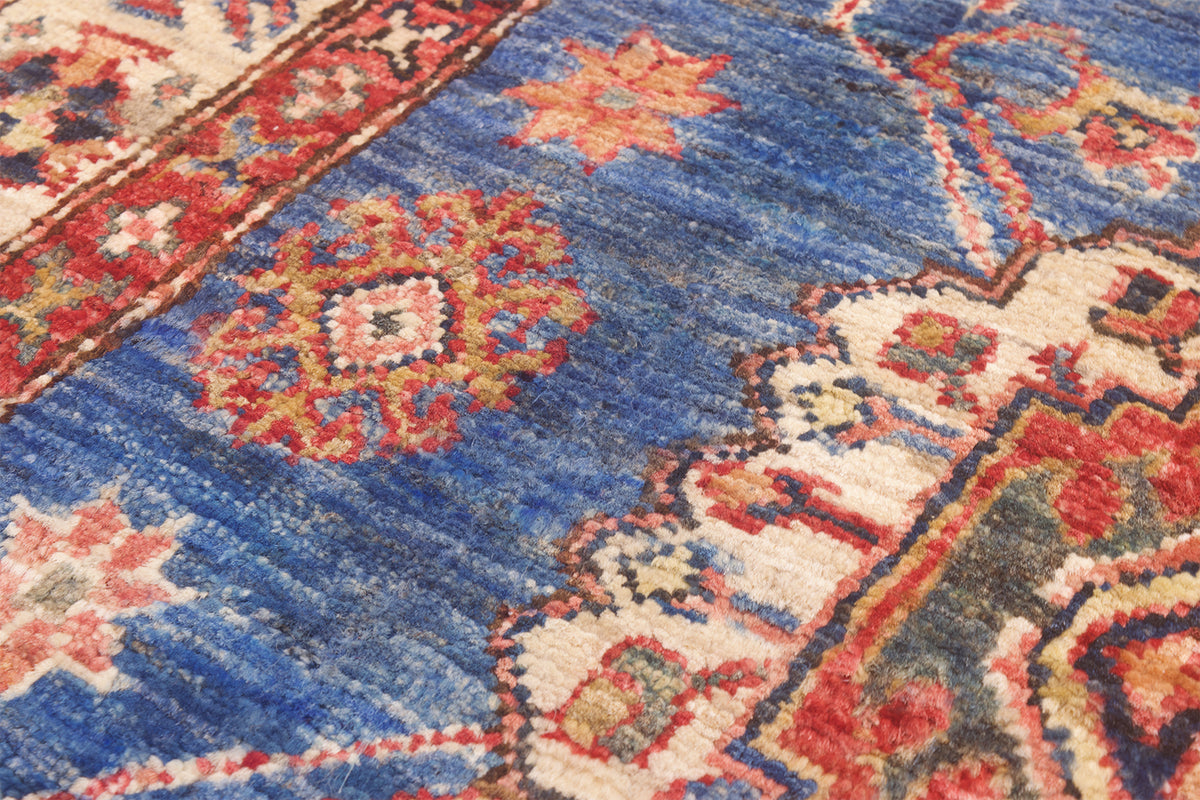A close-up of a traditional patterned Afghan kazak design rug with a dominant medium blue field, featuring red, beige, and orange floral medallions and geometric borders.