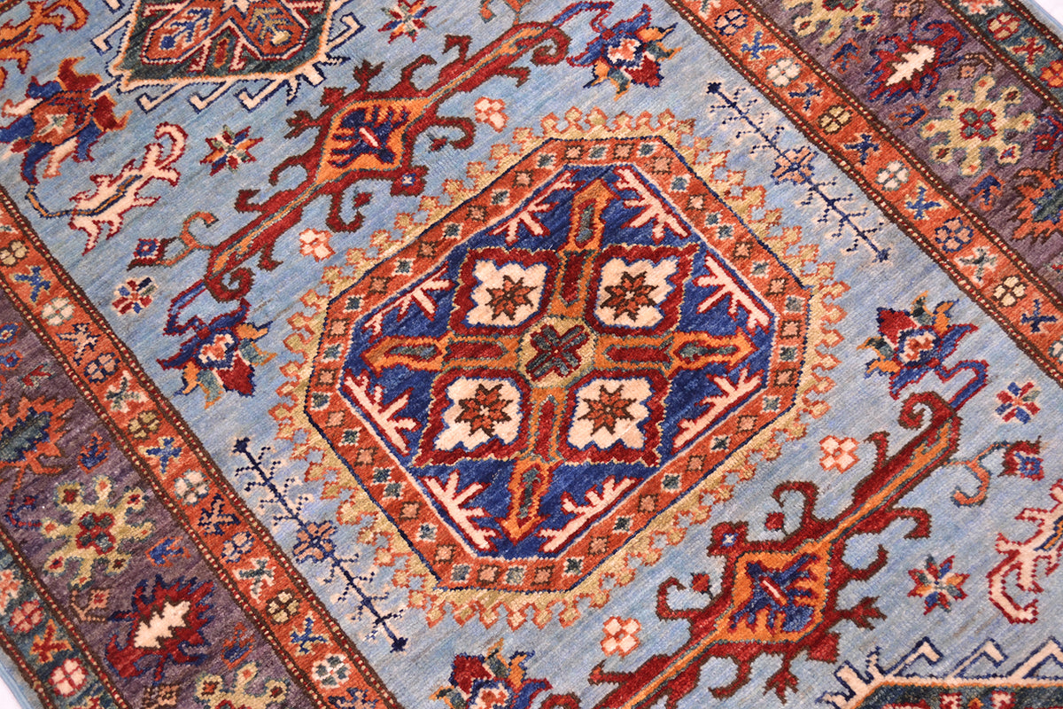 A close-up of a traditional patterned rug featuring a central medallion with blue, red, beige, and orange motifs on a light blue field.