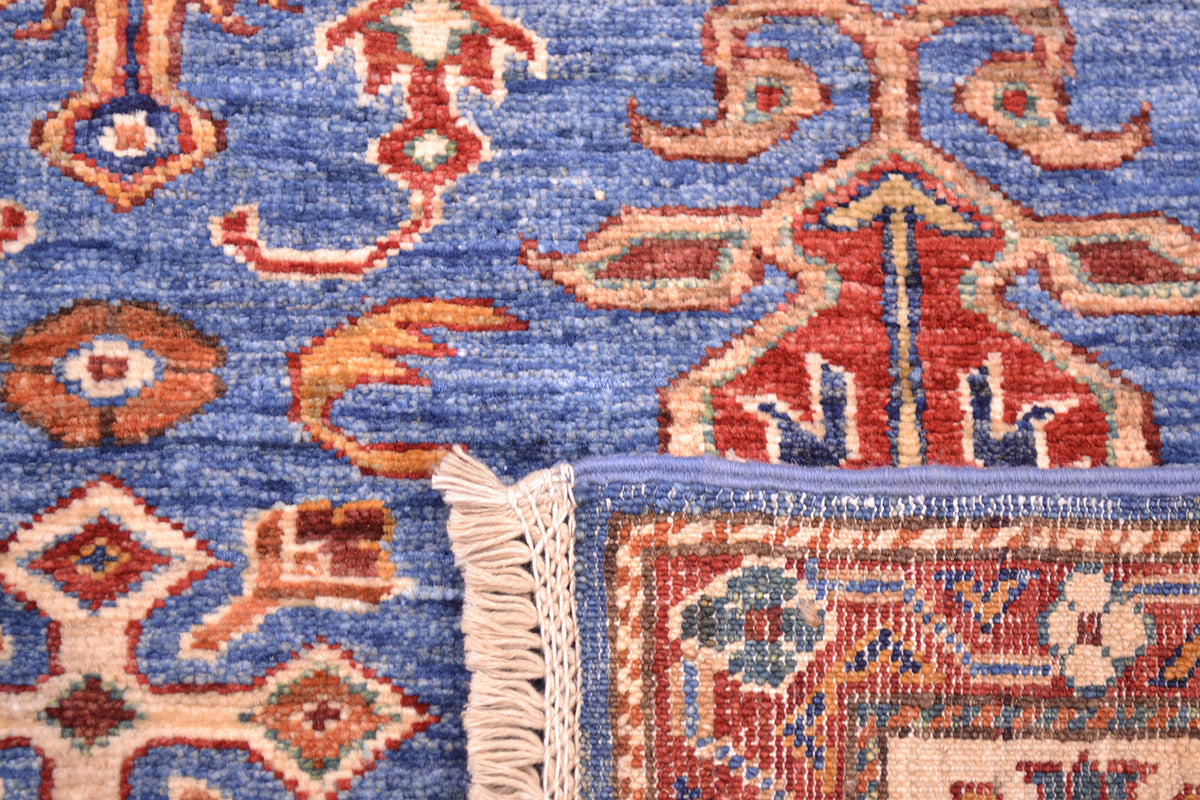 Close-up of a patterned area rug with a blue field, red and beige ornamental motifs, and cream fringe along the edge.
