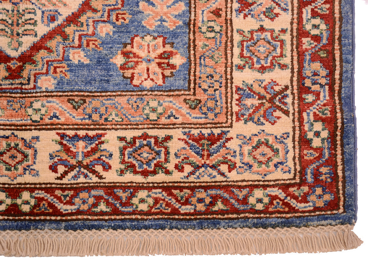 A close-up of a traditional patterned handmade Afghan Kazak small rug corner showing a blue field and three borders in soft orange, beige and rust-red.