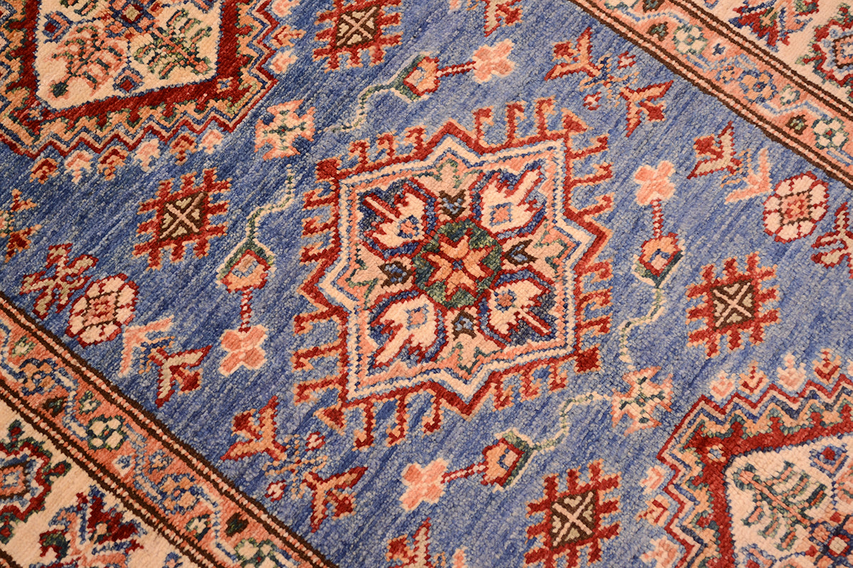 A close-up of a traditional patterned fine Kazak Afghan small rug featuring a blue field with red, beige, and green geometric and floral motifs.