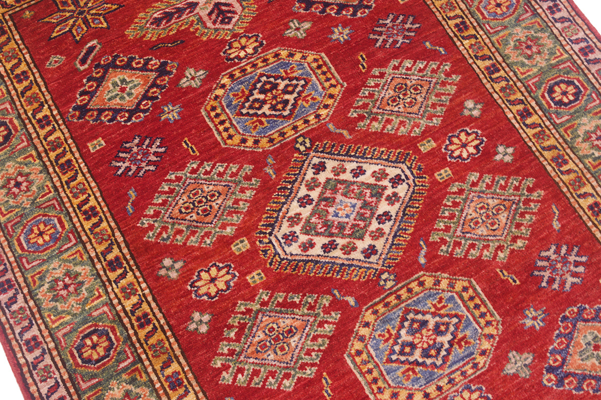 A close-up of a Fine red handmade Afghan Kazak Rug with a dominant red field, featuring geometric medallions and floral motifs in beige, blue, green, and orange.