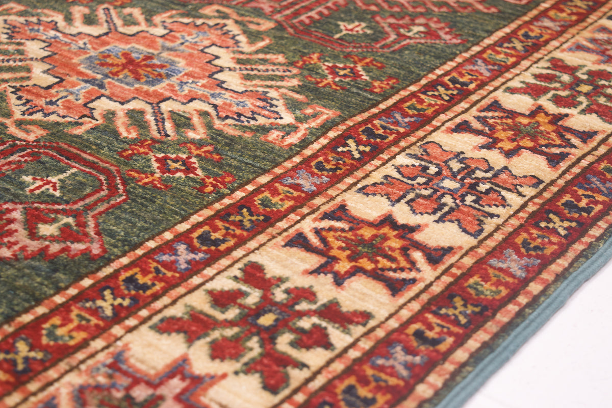 A close-up of a traditional patterned Afghan Kazak hallway Runner showing a green field with red, beige, and blue geometric motifs and a detailed border.