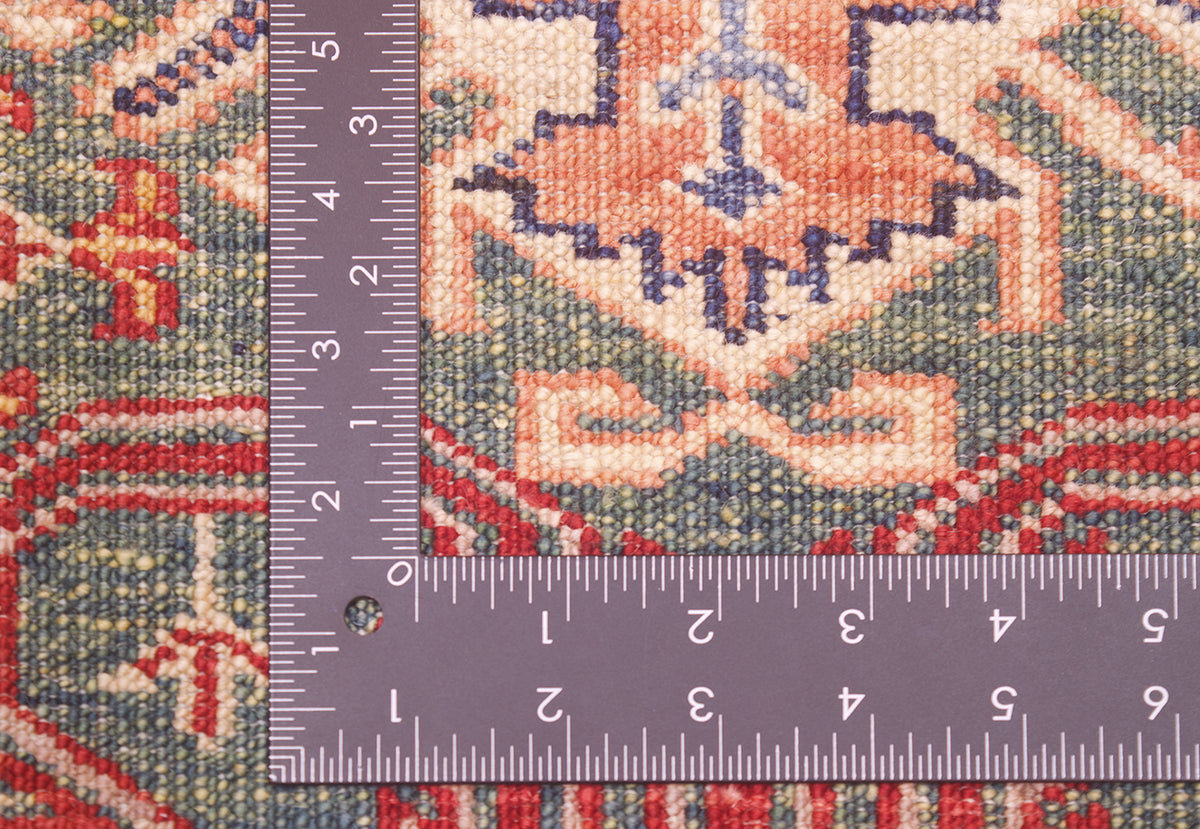 Close-up of the knotted weave of fine handmade green Afghan Kazak Runner with a metal L-shaped ruler showing measurements in inches to help show scale.