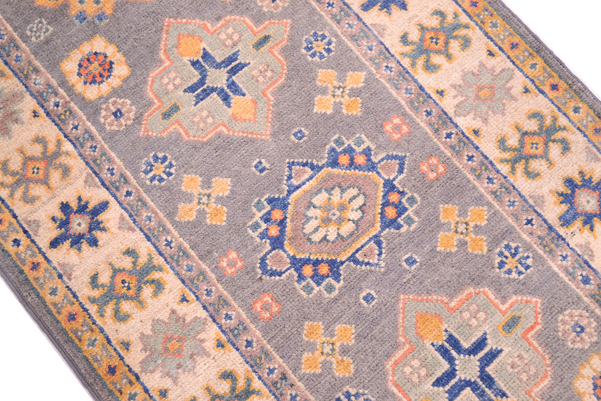 A close-up of a woven grey Handmade Kazak Strip with a geometric and floral medallion pattern in grey, beige, blue, and orange.