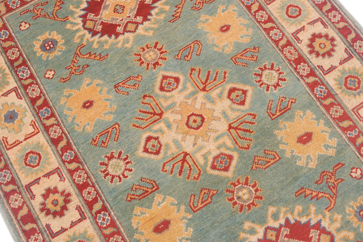 A close-up of a patterned Afghan Kazak rug with a light seafoam green field, red and orange geometric motifs, and cream borders.