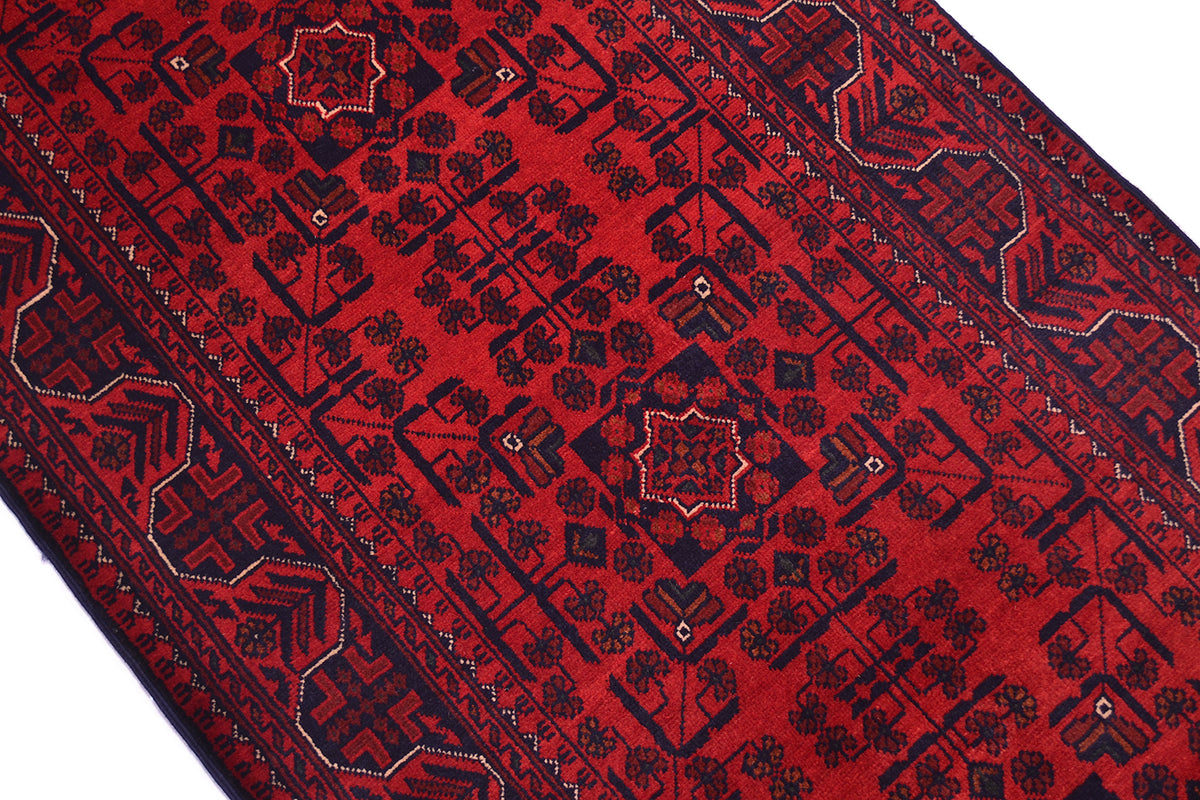 A close-up of a red patterned rug with dark navy geometric and floral motifs, shown diagonally against a white background.
