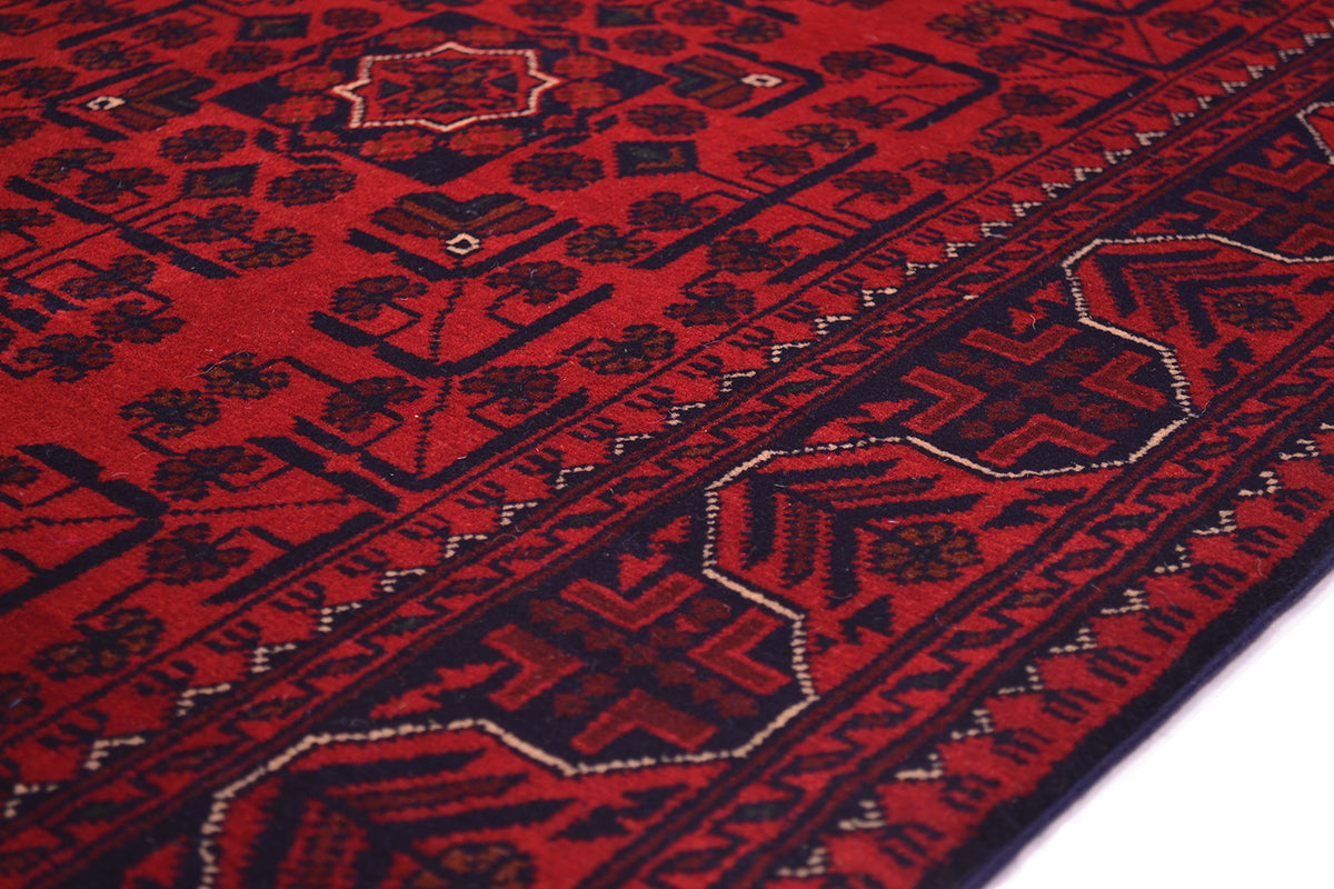 A close-up of a red and black patterned runner rug with geometric and floral motifs, showing the detailed woven texture and border design.