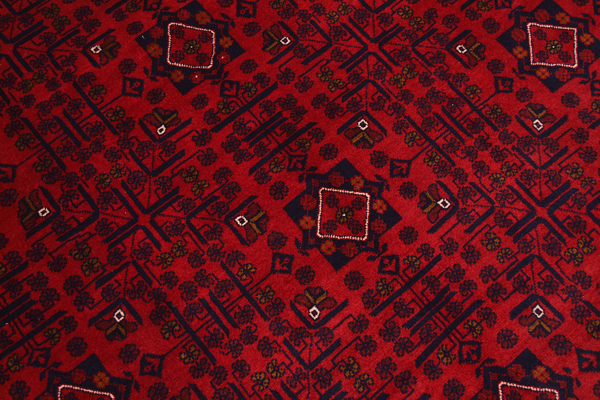 A close-up of a red afghan patterned rug featuring dark navy geometric and floral motifs with small white accents.