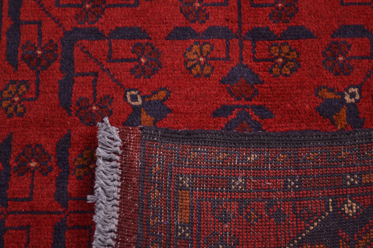 Close-up of the knots on back of red afghan rug with dark navy floral motifs and a fringed edge, showing the woven texture and part of the border design.