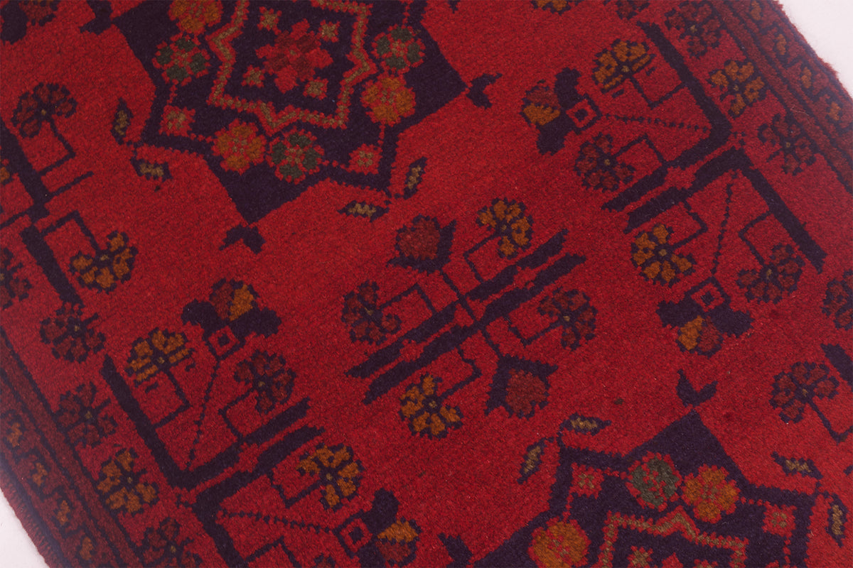A close-up of a red patterned afghan rug with dark navy geometric and floral motifs.