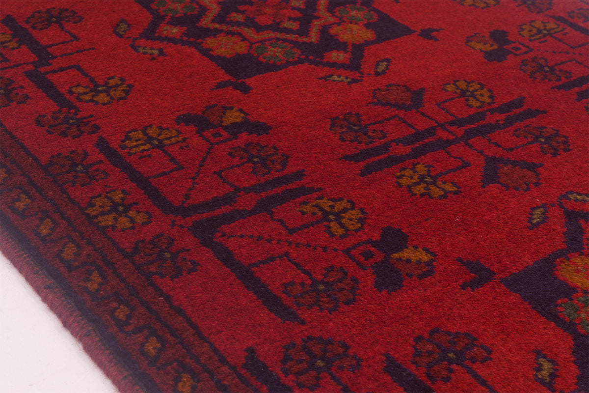 A close-up of a red patterned afghan rug with dark navy and mustard yellow geometric and floral motifs.