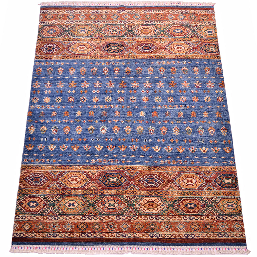 A rectangular Khurjeen area rug with a traditional geometric pattern, featuring a prominent blue center field bordered by rust orange and beige bands with intricate diamond and floral motifs.