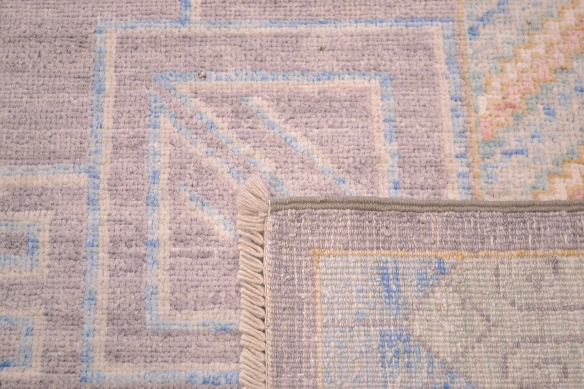 Reverse of Khotoan design carpet in grey, cream, green, gold and pink showing handknotting and cotton warp fringes.