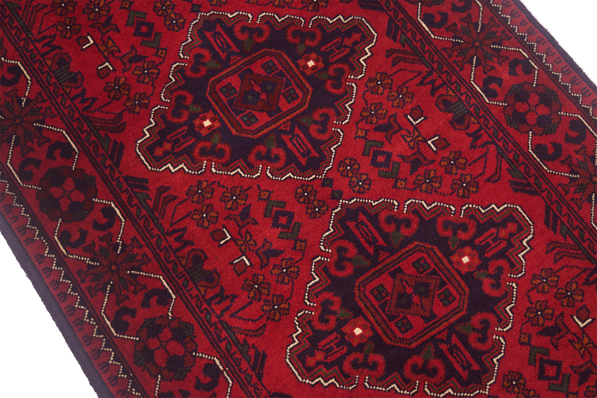 A close-up of a traditional patterned afghan rug with a deep red field, dark navy blue medallions and borders, and small cream accents.